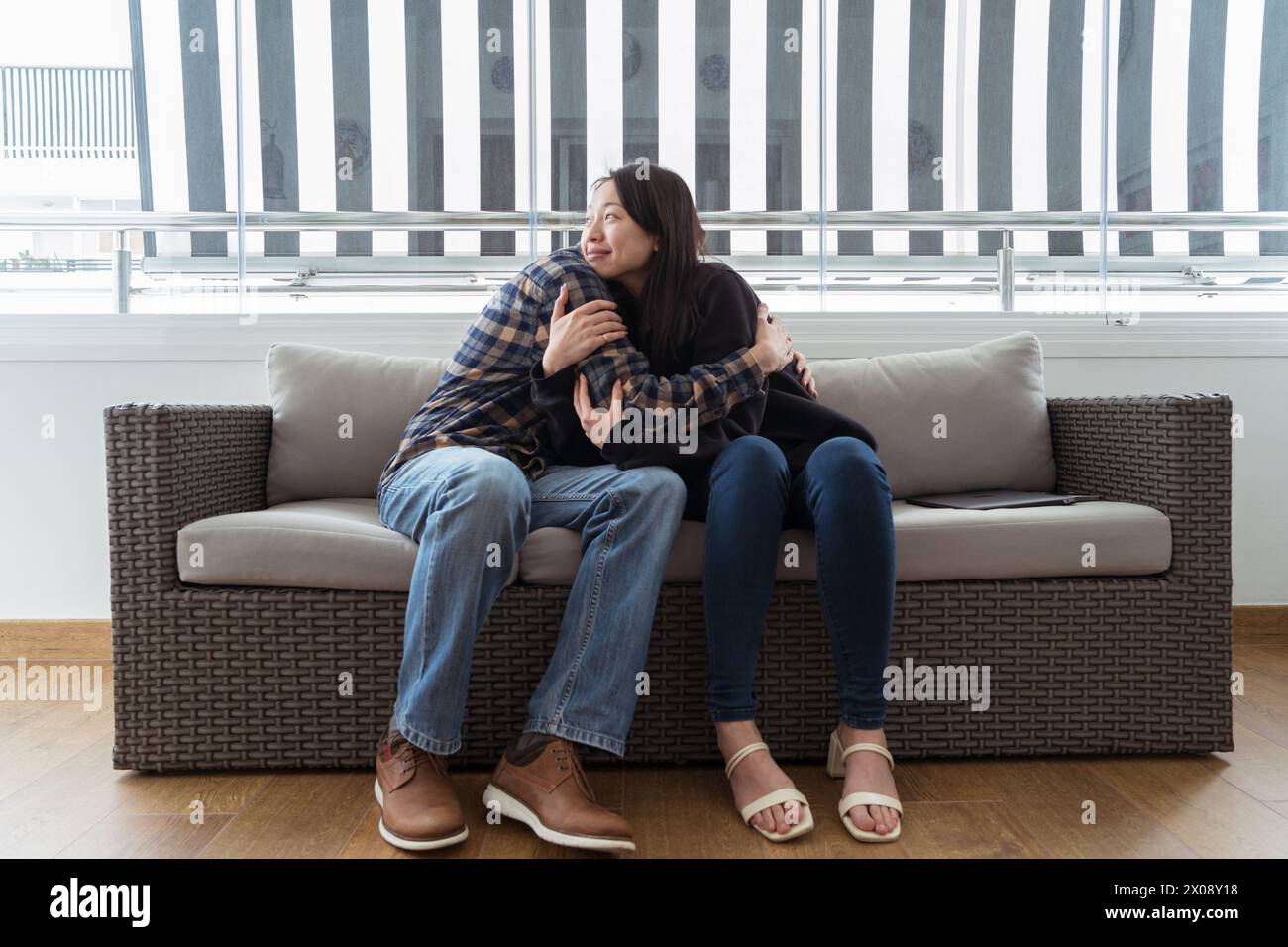 Una donna asiatica e un uomo caucasico si abbracciano su un divano mostrando amore e compagno in tutte le culture Foto Stock