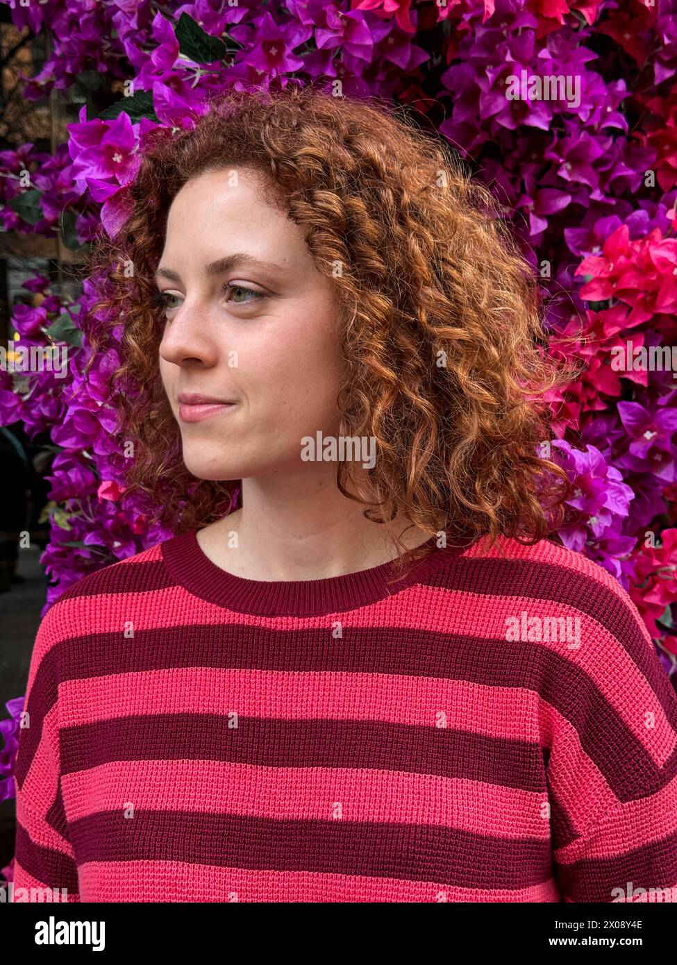 La giovane donna rossa con i capelli ricci si trova di fronte a una vivace bouganville Foto Stock