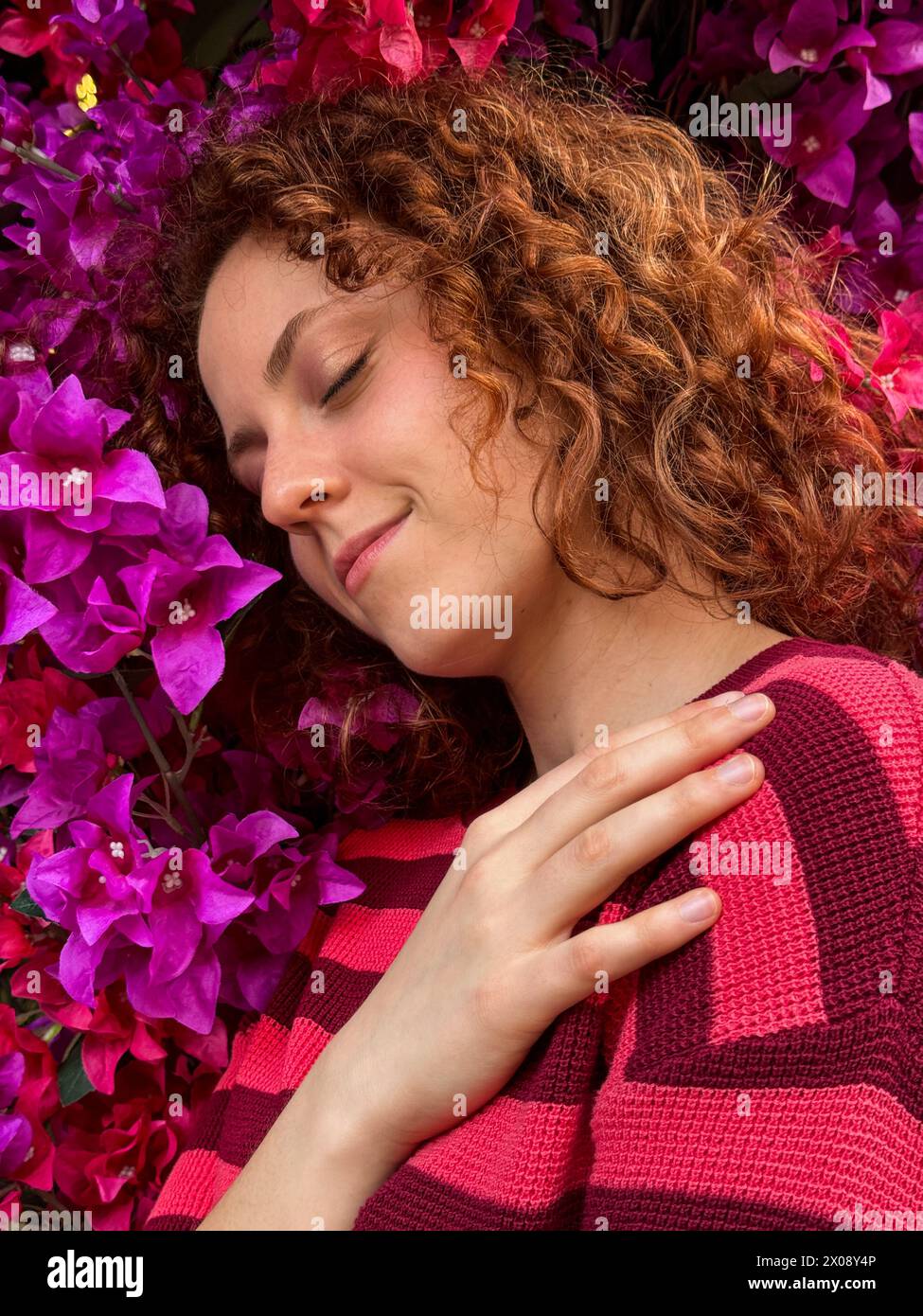 Una giovane donna rossa con capelli ricci gode un momento di pace circondato da vibranti fiori rosa Foto Stock