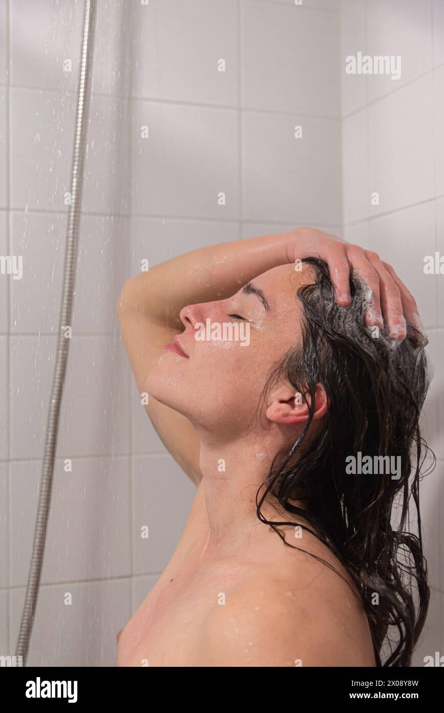 Una donna viene catturata in un momento di relax mentre l'acqua scorre sopra di lei, lavando lo shampoo dai suoi capelli durante la doccia Foto Stock