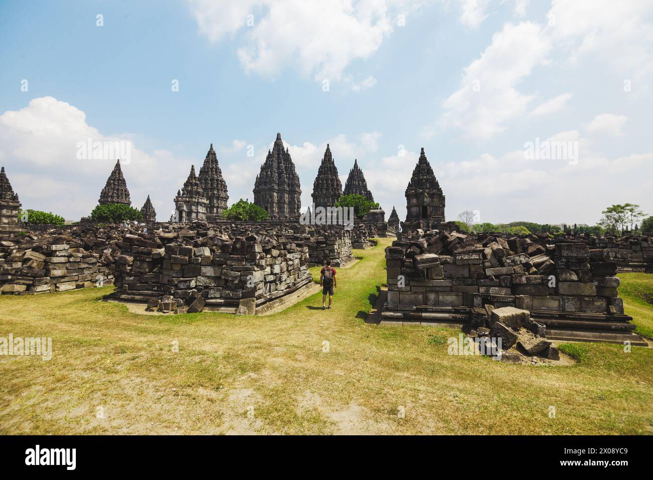 Un viaggiatore si aggira attraverso le antiche rovine del Tempio di Prambanan, un sito patrimonio dell'umanità dell'UNESCO in Indonesia, sotto un cielo limpido Foto Stock