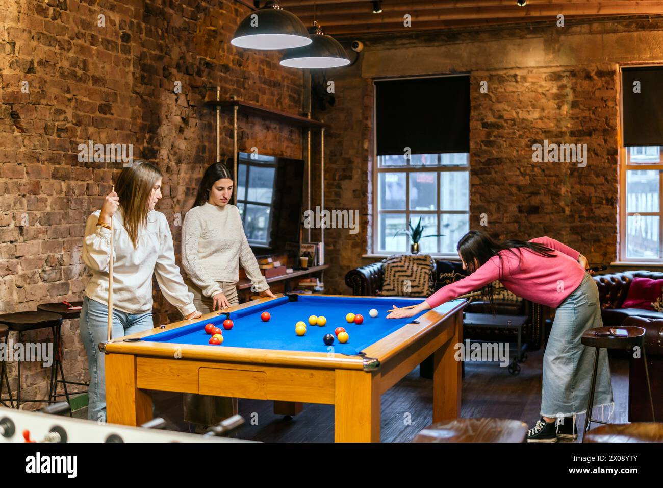 Le giovani amiche si divertono a giocare a biliardo in un intimo interno con pareti in mattoni Foto Stock