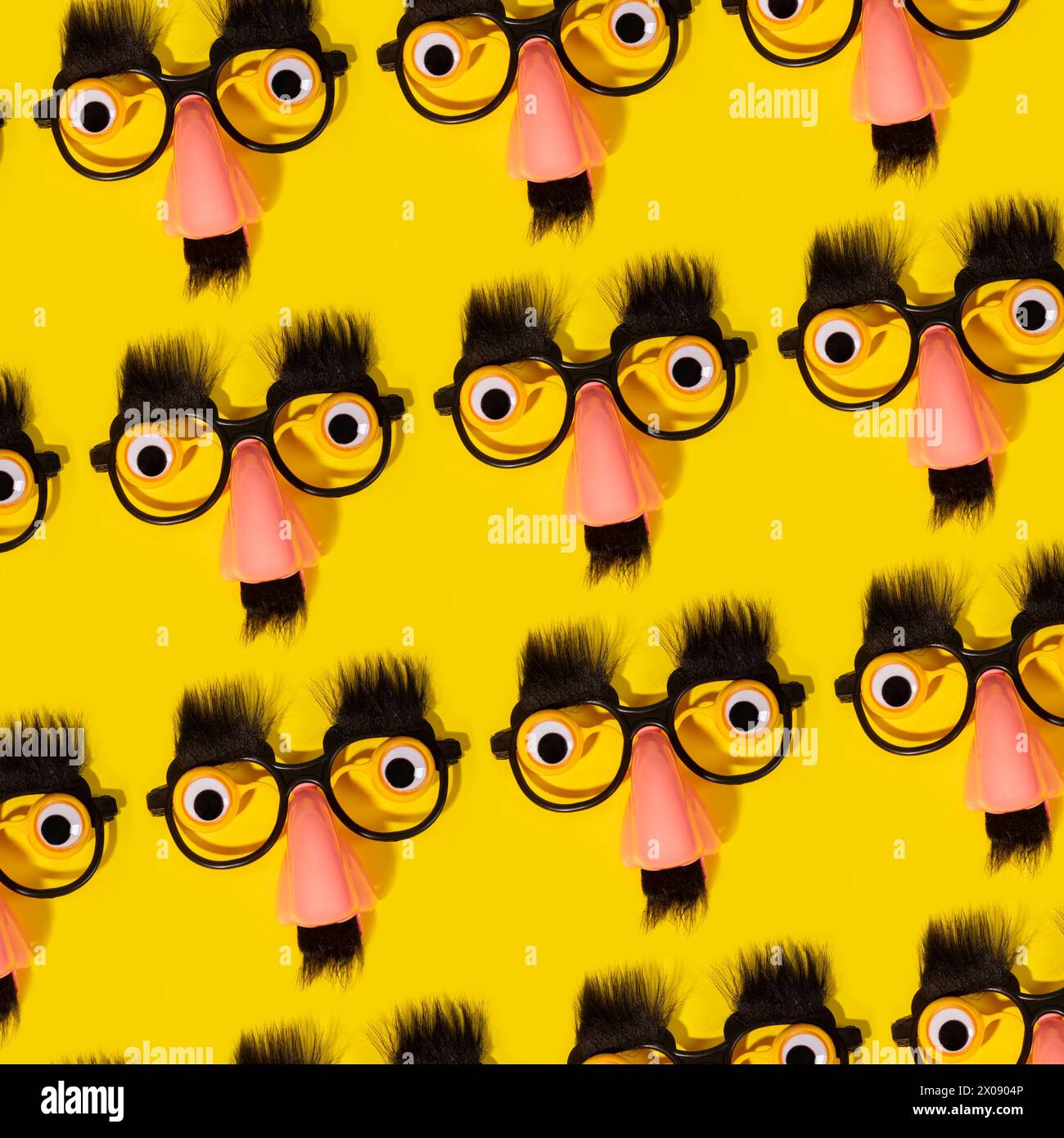 Una serie di finti occhiali comici con naso, baffi e sopracciglia su uno sfondo giallo vibrante, creando un motivo eccentrico. Foto Stock