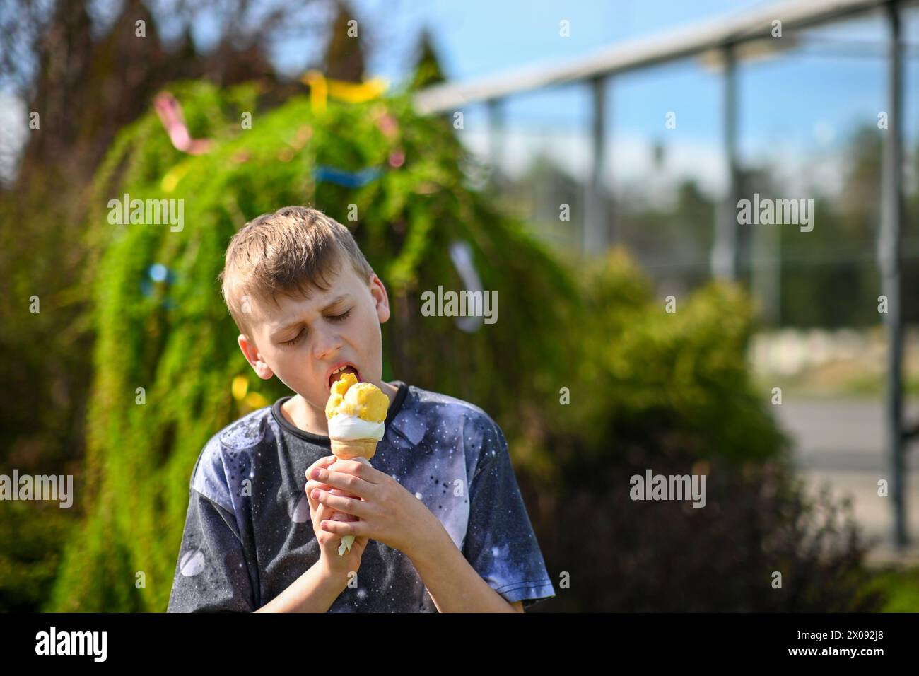 il bambino di 10 anni lecca il gelato, sfondo sfocato di un albero. Foto Stock