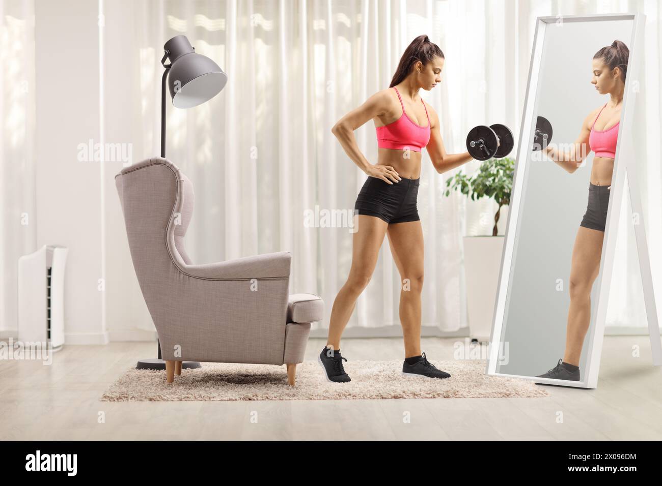 Adatta la giovane donna che esercita l'allenamento con il peso con un manubrio davanti a uno specchio a casa Foto Stock