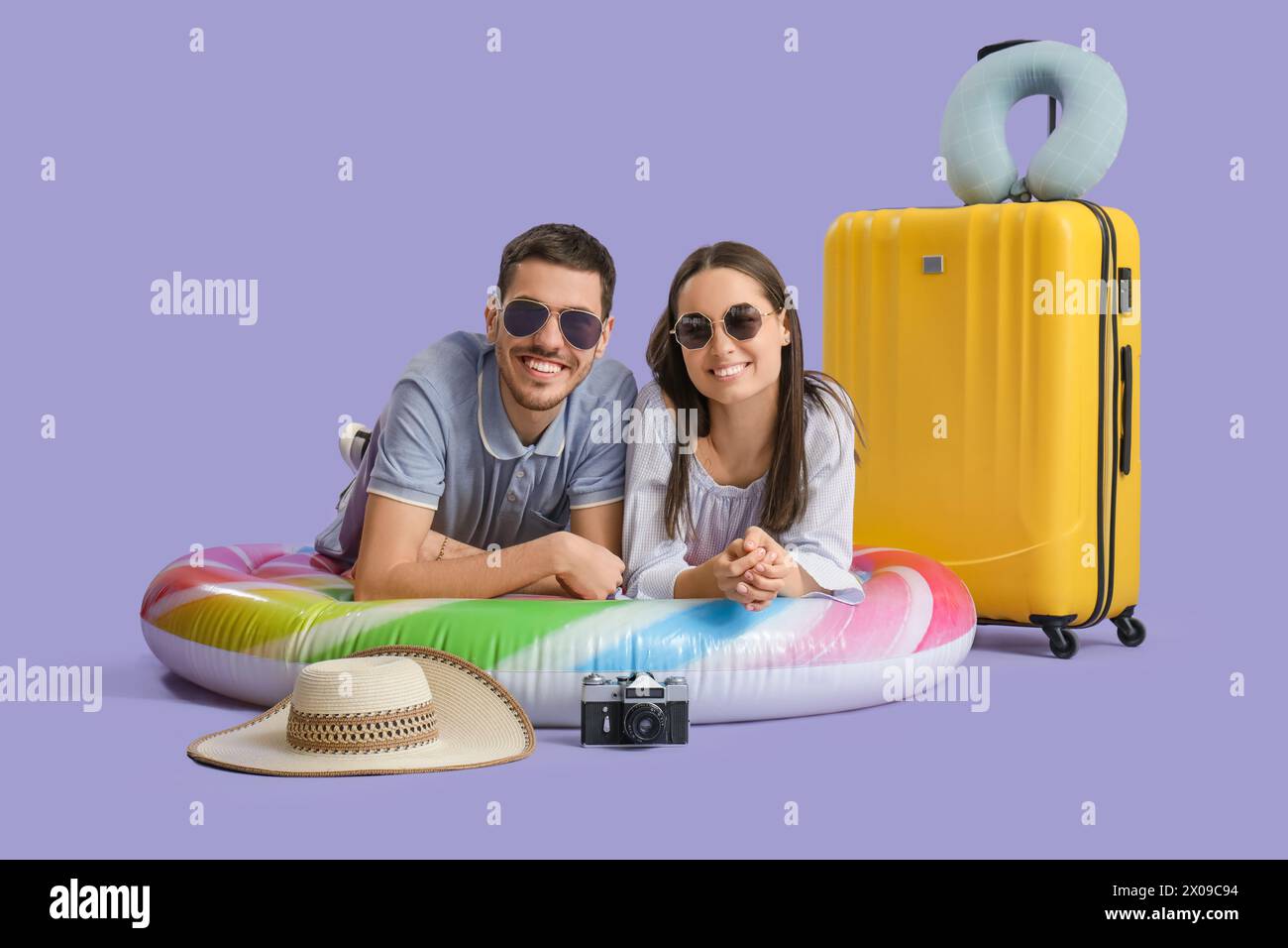 Bella giovane coppia felice di turisti con valigia, materasso gonfiabile e macchina fotografica su sfondo viola Foto Stock