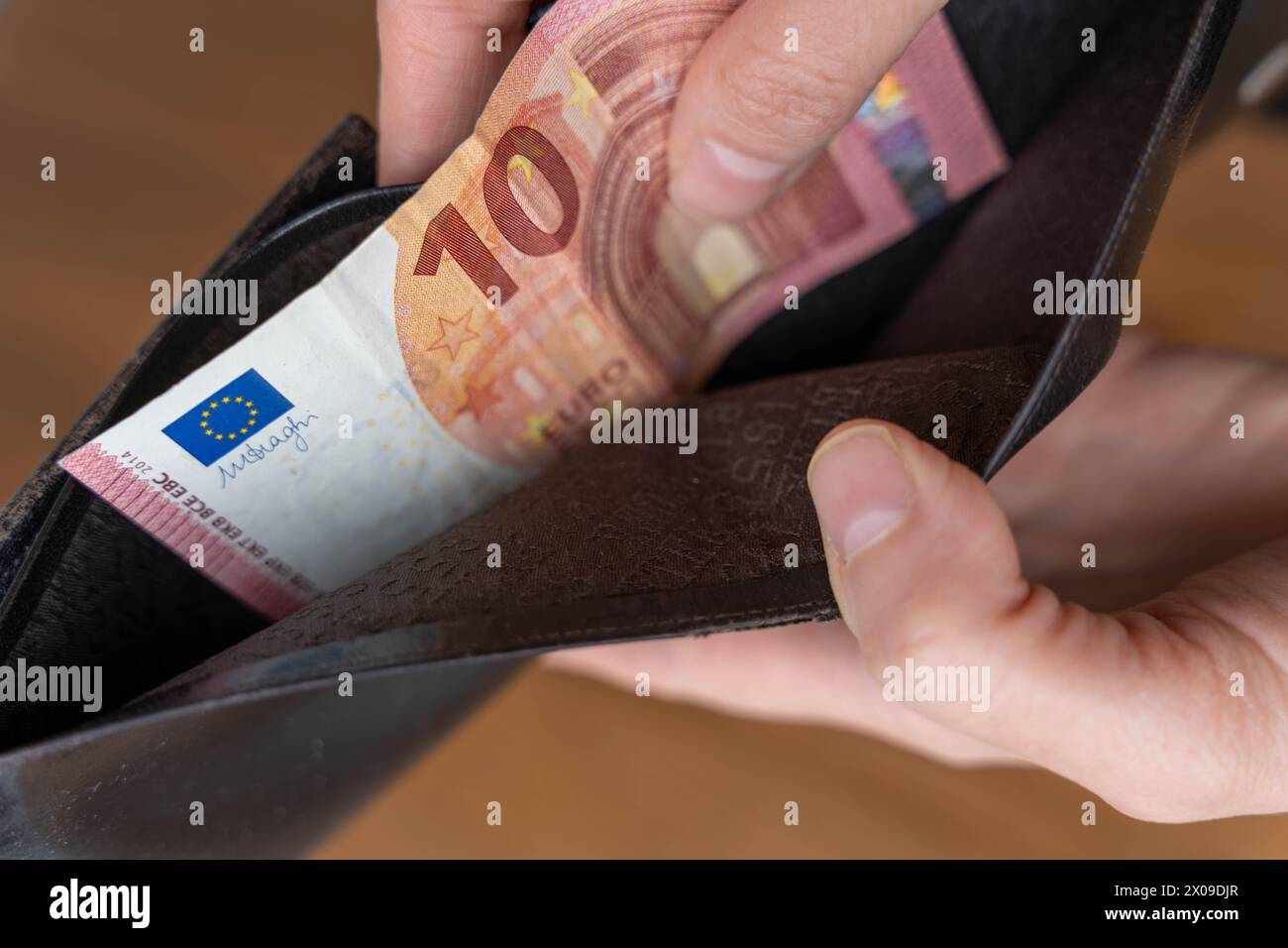 Una persona inserisce moneta cartacea in un portafoglio nero in pelle, concentrandosi sul semplice atto di garantire le risorse finanziarie. Foto Stock