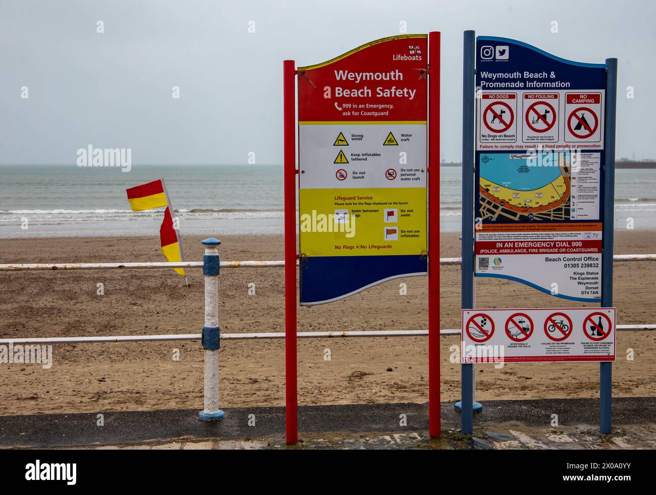 Weymouth Beach Safety and Information board con bandiere bagnino che soffiano al vento in una giornata coperta e umida ad aprile. Foto Stock