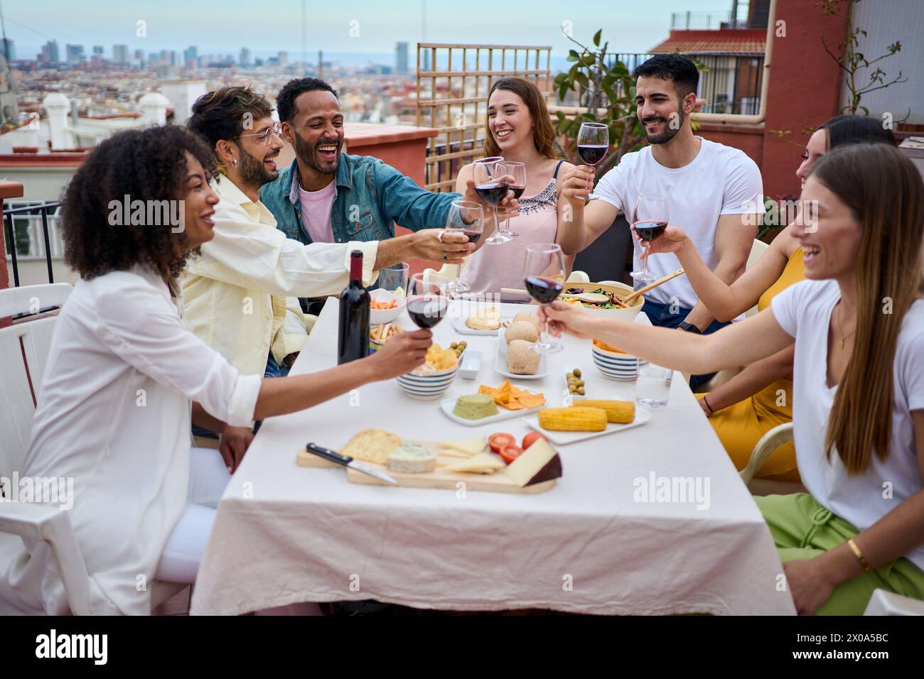 Gruppo di giovani felici che brindano vino rosso e festeggiano il pasto sul tetto Foto Stock