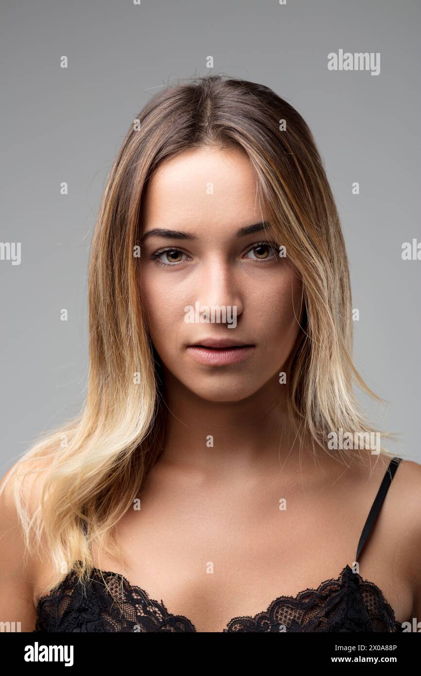 Catturata dal petto in alto, la parte superiore in pizzo e i capelli chiari della donna incorniciano la sua espressione sincera e introspettiva Foto Stock