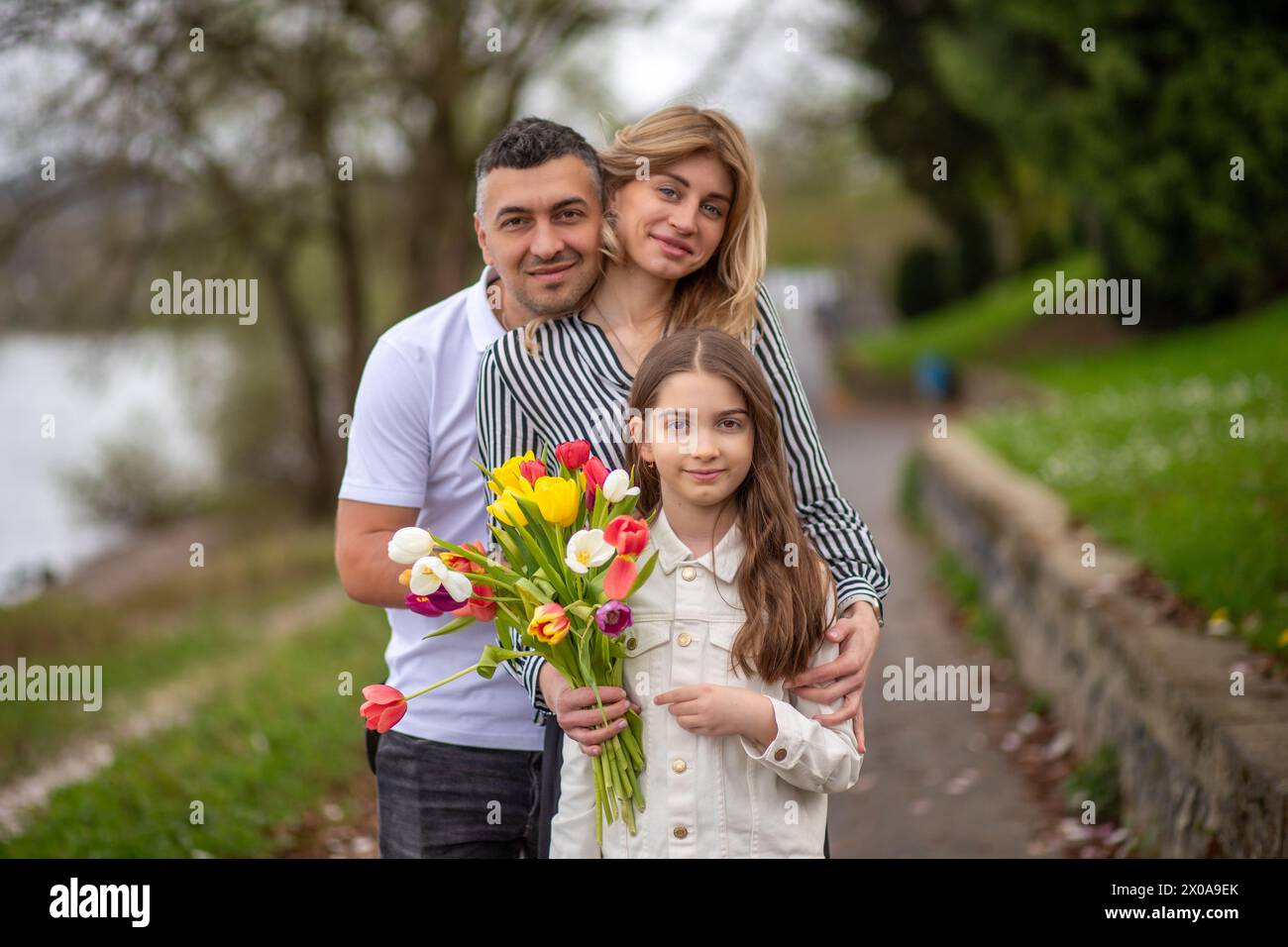 Famiglia di tre persone, uomo, donna e ragazza con tulipani che godono del tempo primaverile nel parco Foto Stock