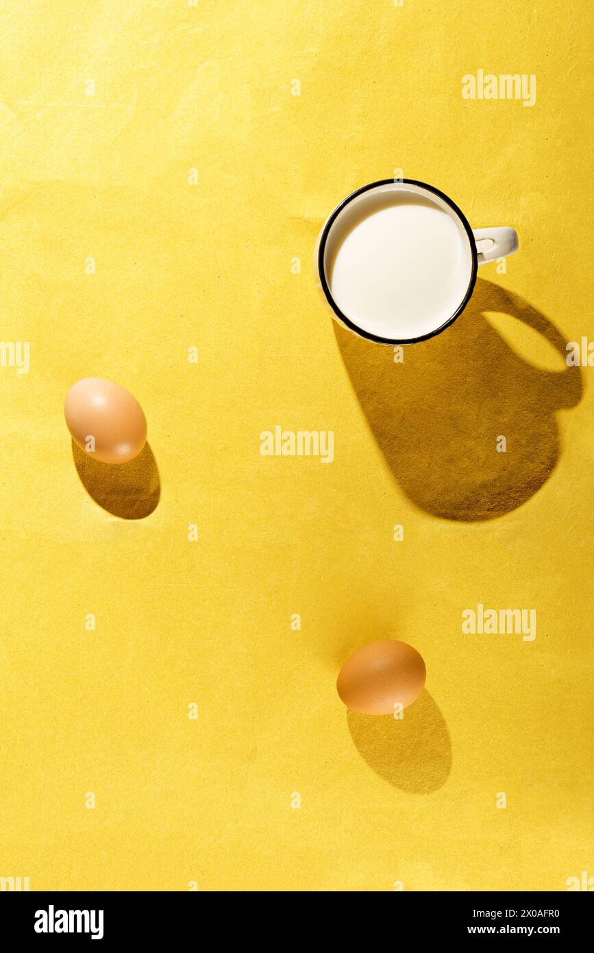 Immagine di natura morta con tazza di latte e uova su sfondo giallo Foto Stock