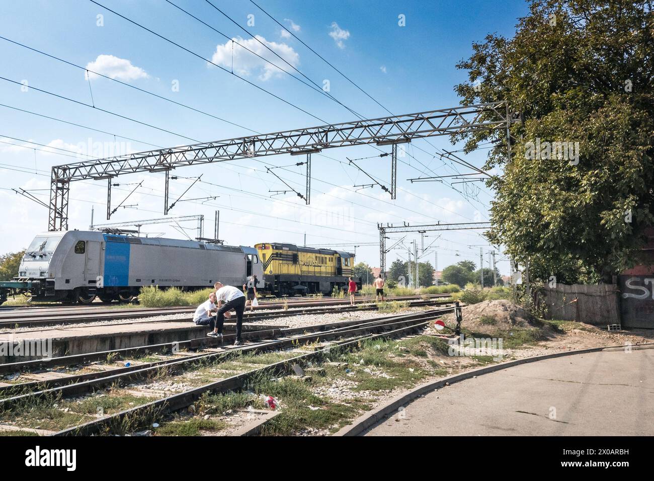 Foto di un popolo che aspetta nella stazione ferroviaria di Batajnica, in Serbia, con un treno merci sullo sfondo Foto Stock