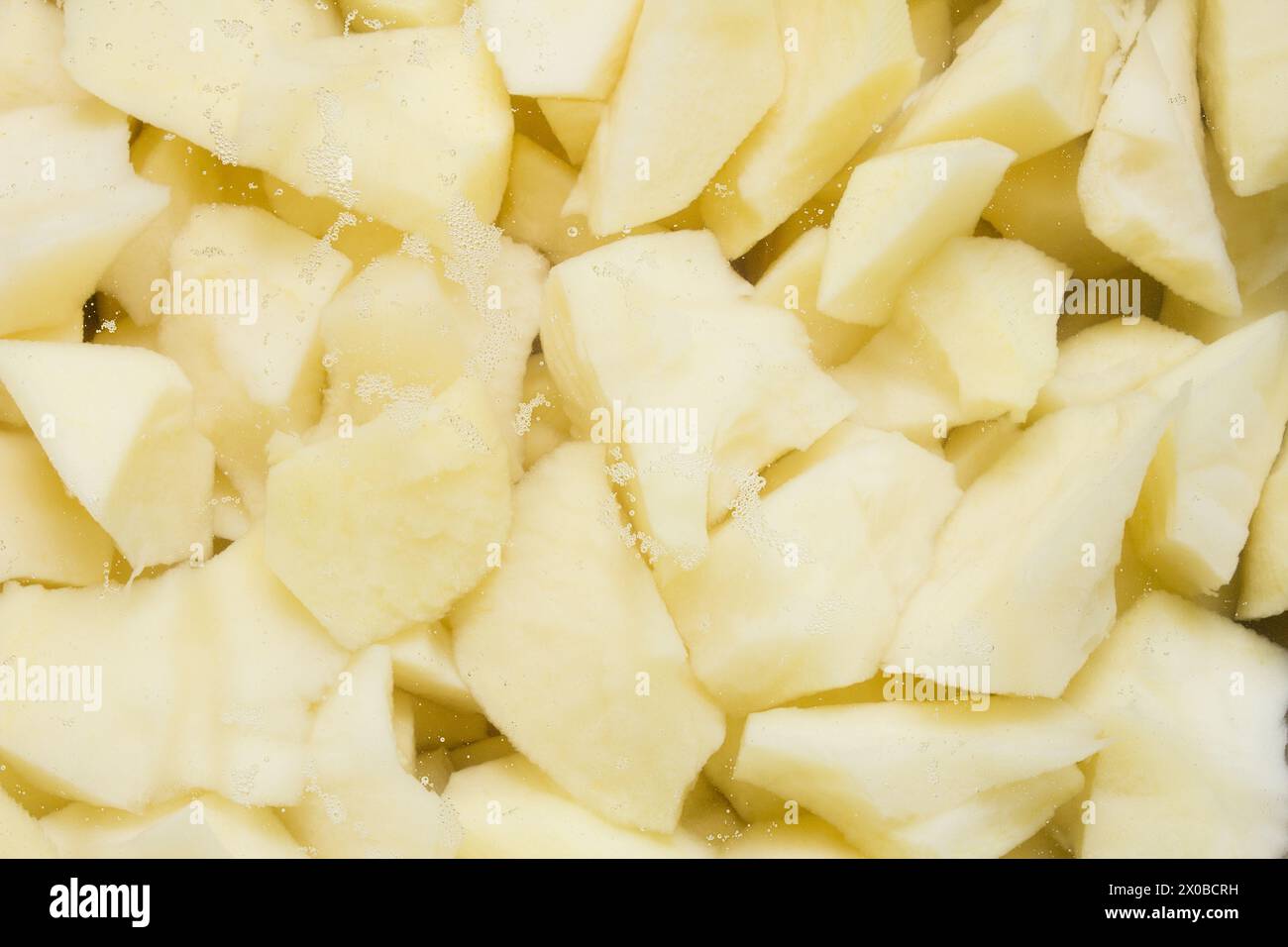 Primo piano di patate crude appena tagliate con piccole bollicine, pronte per la cottura. Preparazione degli alimenti. Foto Stock
