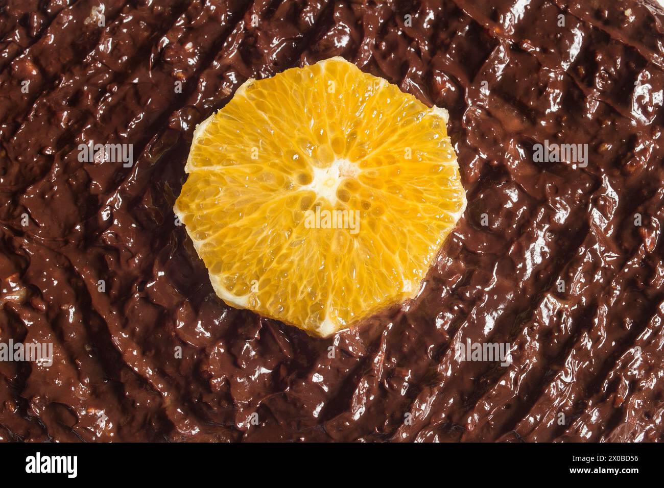 Vista dall'alto di una fetta di arancione giallo brillante e vivace su uno sfondo di cioccolato lucido e testurizzato. Il contrasto e la distensione dei colori Foto Stock