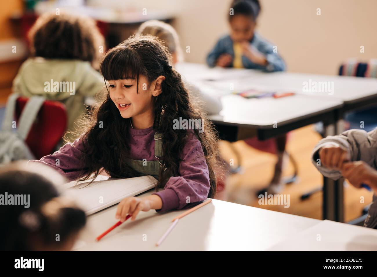 Studentessa della scuola elementare seduta alla sua scrivania e a fare il suo lavoro scolastico. Scolarizzazione femminile in un centro di sviluppo bambini co-ed. Foto Stock