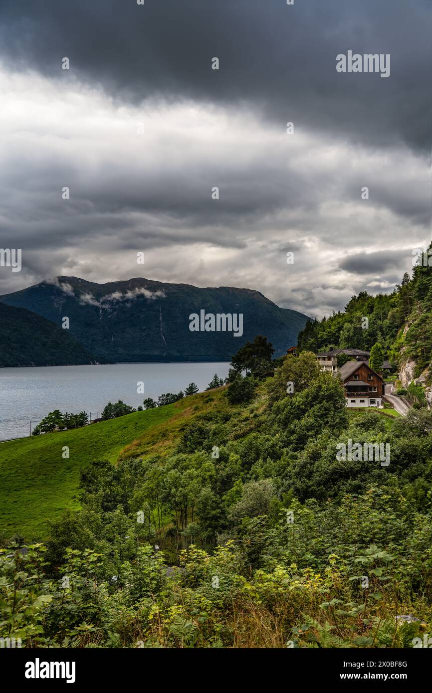 Villaggio norvegese dei fiordi con nuvole scure in estate. Un tranquillo villaggio nordico incastonato lungo il Tingvollfjorden, che sovrasta le montagne Foto Stock