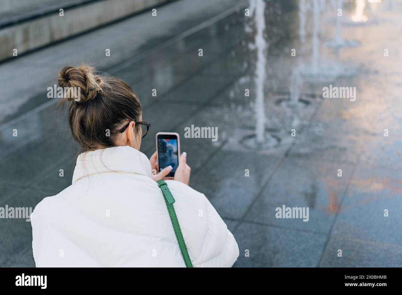 Donna che scatta foto della fontana con il telefono cellulare mentre cammina per la città Foto Stock