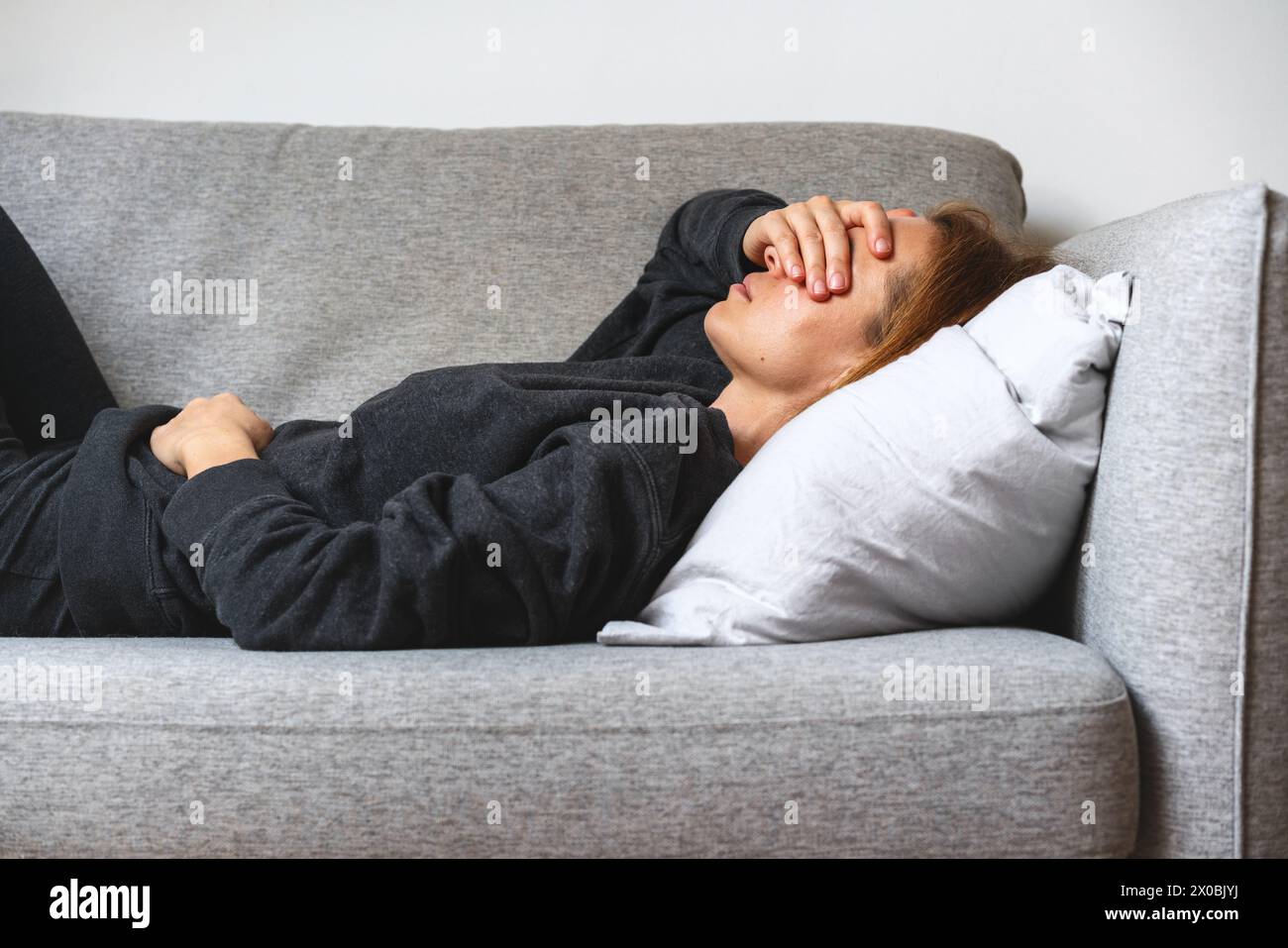 Infelice disperata depressa donna sdraiata sul divano e che copre gli occhi con la mano. Foto Stock