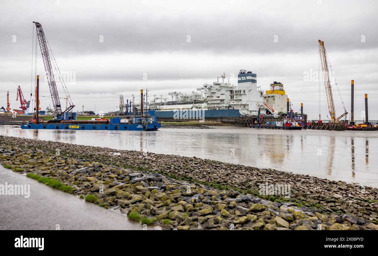 11 aprile 2024, Schleswig-Holstein, Brunsbüttel: I lavori di costruzione del nuovo molo per il terminal galleggiante per il gas naturale liquefatto "Jetty" nel porto dell'Elba di Brunsbüttel partono da un pontile galleggiante accanto alla nave speciale per lo stoccaggio e l'immissione di gas naturale liquefatto "Hoegh Gannef", a cui è ormeggiata la nave da trasporto a GNL "TEnergy". Foto: Axel Heimken/dpa Foto Stock