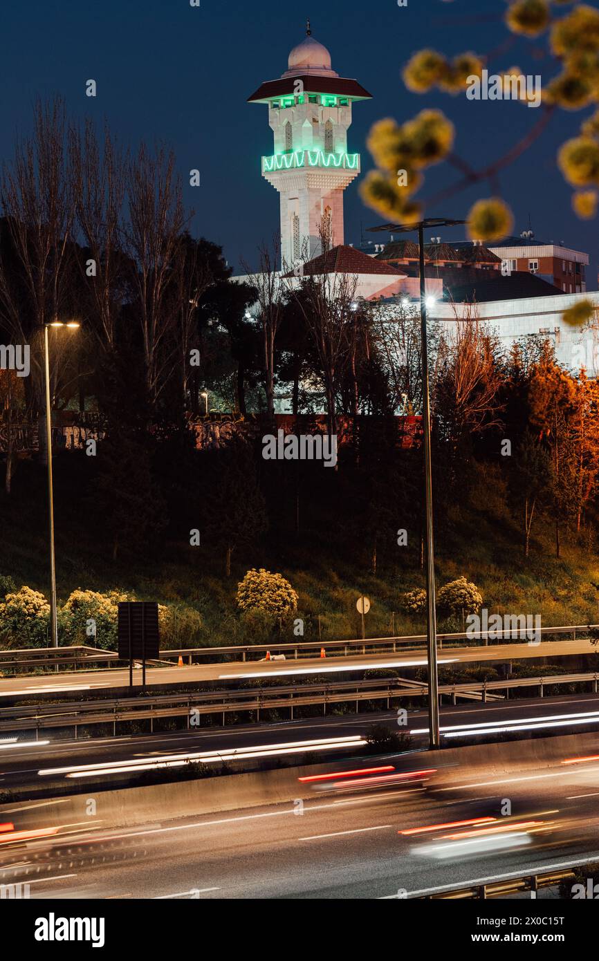 Una maestosa moschea bianca con un torreggiante minareto illuminato perfora il cielo notturno, con le sue finestre che si illuminano di luce calda. Dopo il Ramadan. Colore verde Foto Stock