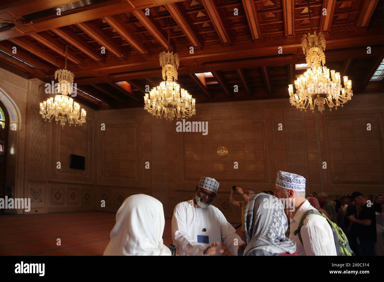 Guida turistica della grande Moschea del Sultano Qaboos con turisti nella sala di preghiera delle donne con soffitto in legno omanita e lampadari di Mascate Oman Foto Stock