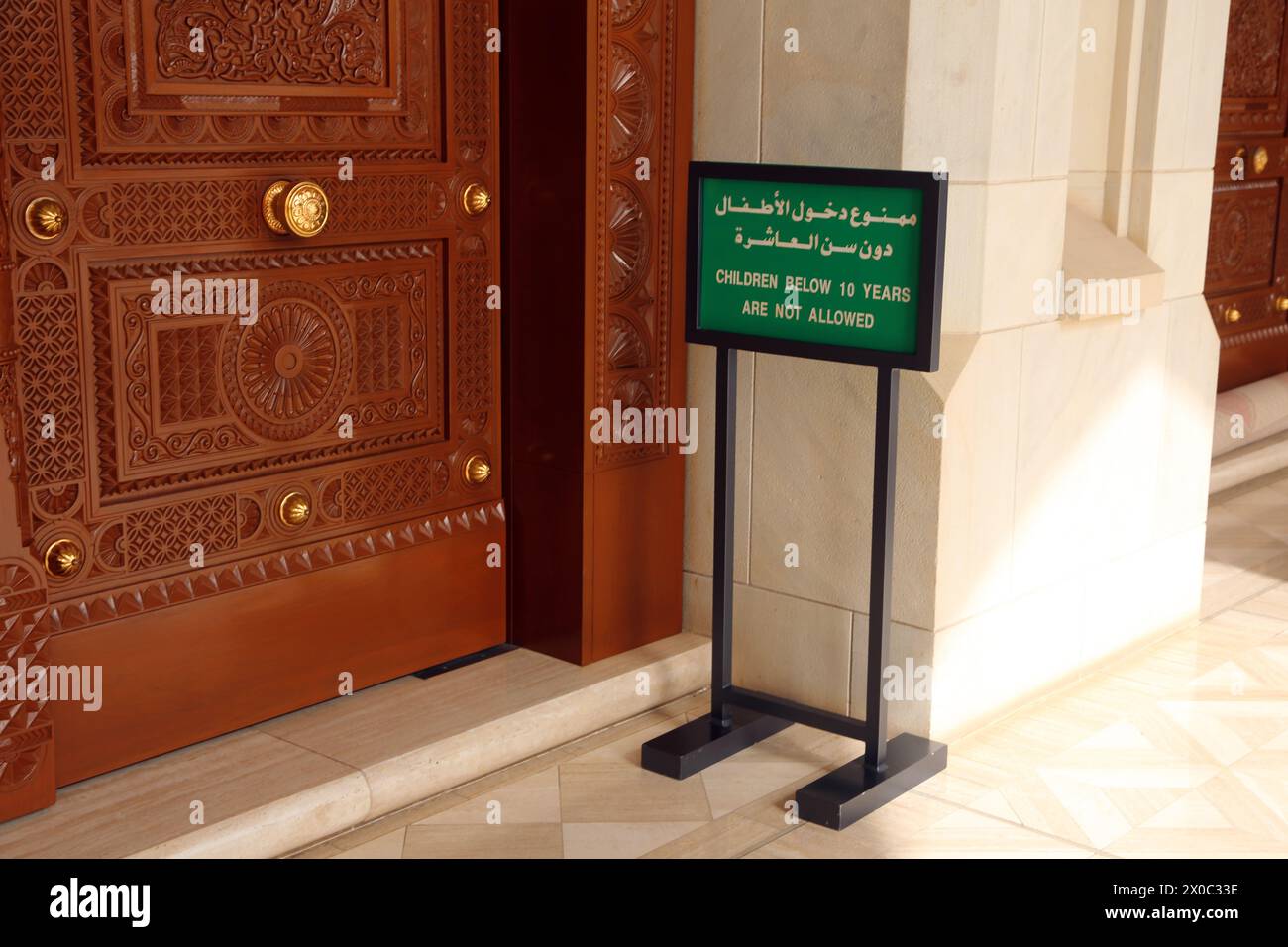 Insegna bilingue interna della grande Moschea del Sultano Qaboos "i bambini al di sotto dei 10 anni non sono ammessi" da porta in legno ornata Muscat Oman Foto Stock Insegna bilingue interna della grande Moschea del Sultano Qaboos "i bambini al di sotto dei 10 anni non sono ammessi" da porta in legno ornata Muscat Oman Foto Stock