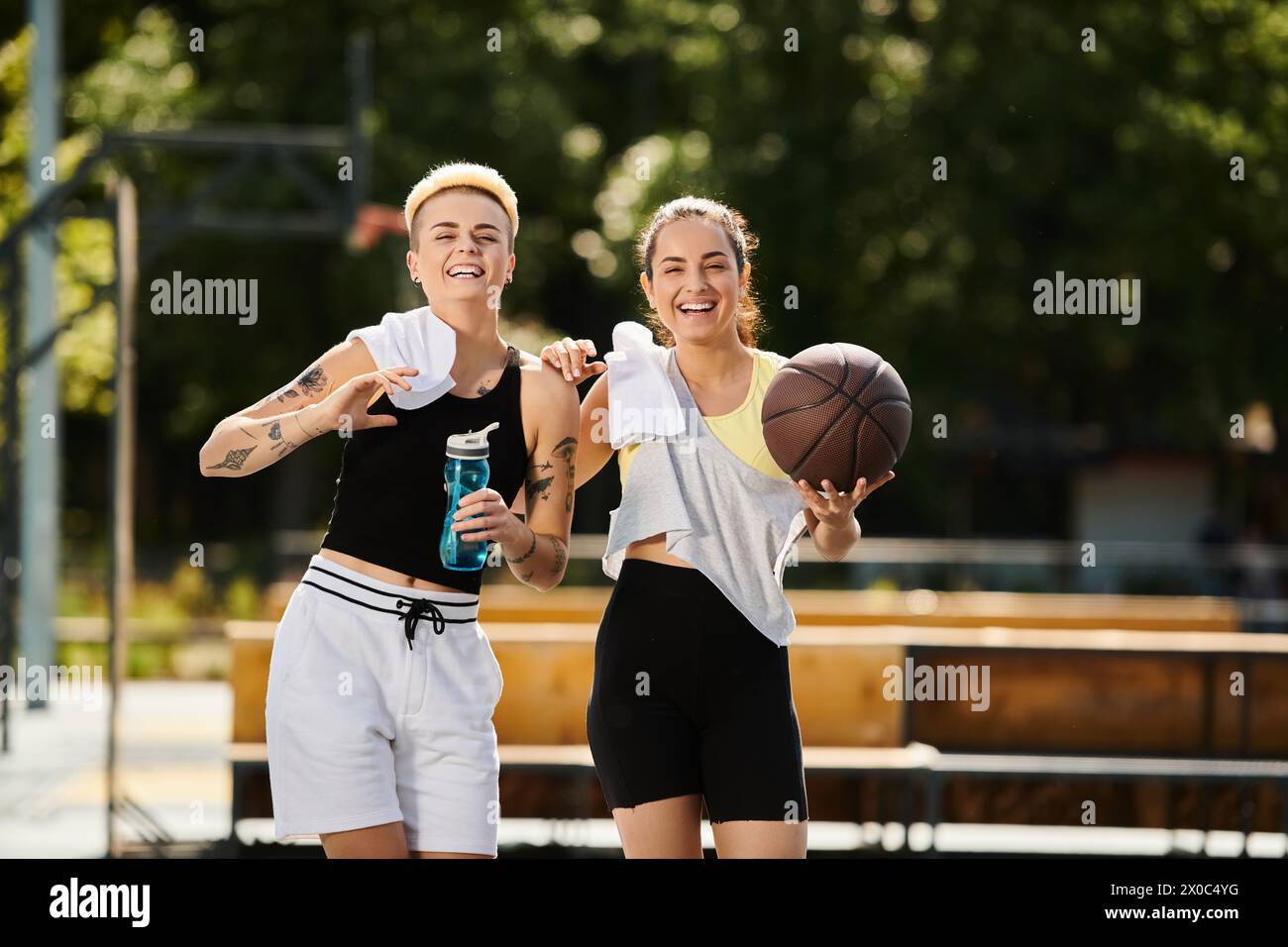 Due giovani donne atletiche che si alzano fianco a fianco con una pallacanestro e si divertono una partita in una giornata di sole all'aperto. Foto Stock
