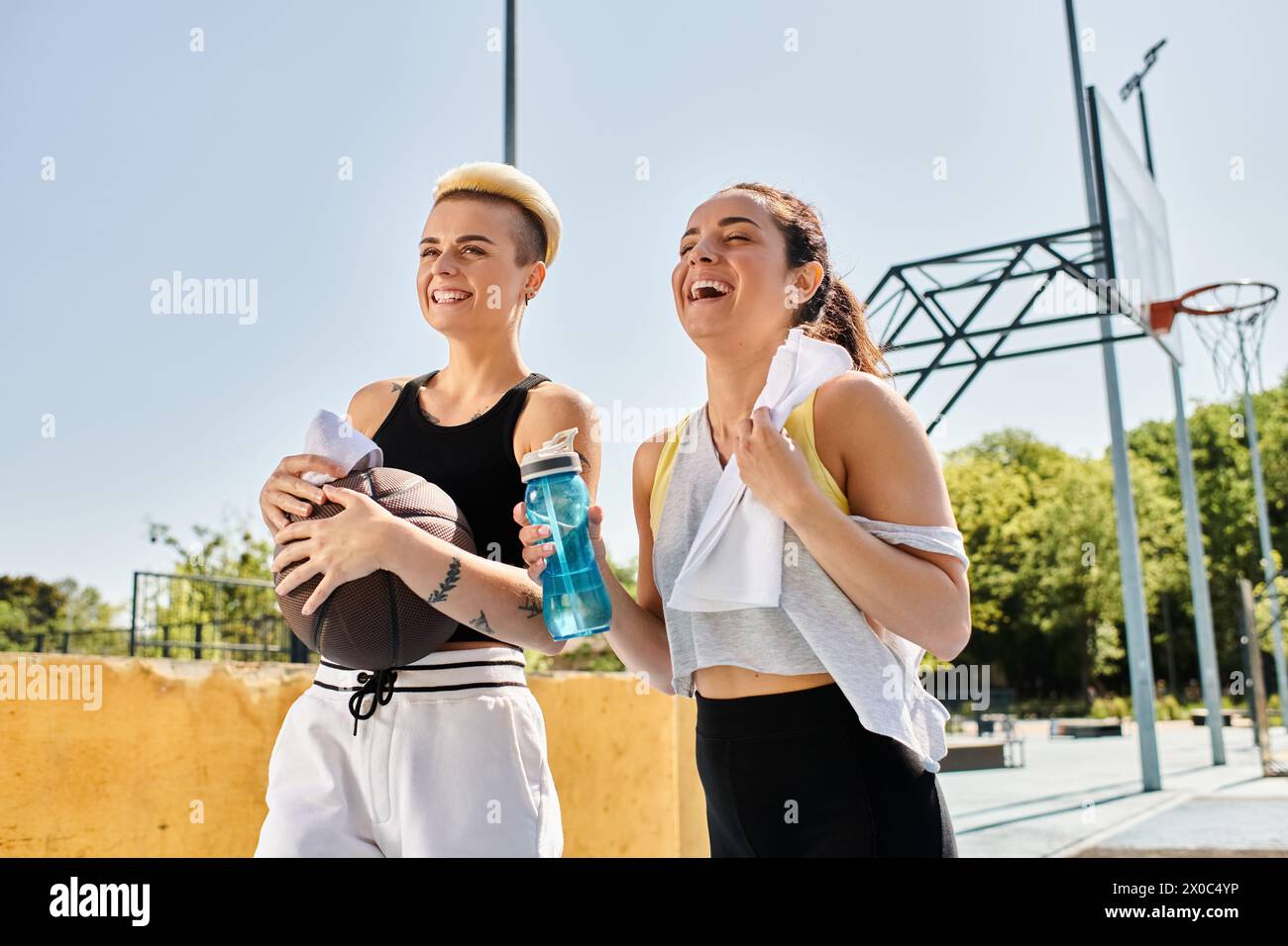 Due giovani donne stanno insieme all'aperto, pronte a giocare a basket sotto il sole estivo. Foto Stock