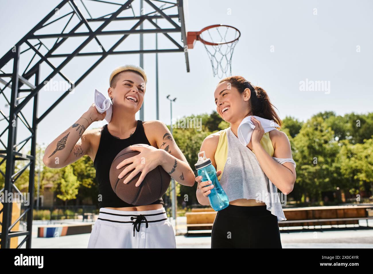 Due giovani donne, amiche, giocano a basket all'aperto in una soleggiata giornata estiva, mostrando il loro atletismo e il loro lavoro di squadra. Foto Stock
