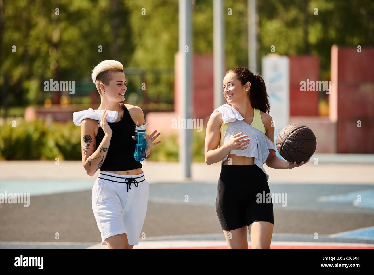 Due giovani donne atletiche si alzano in cima a un campo da basket, incarnando forza e lavoro di squadra in un ambiente estivo. Foto Stock