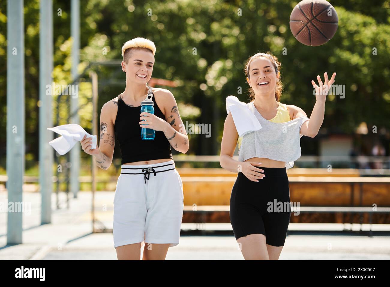 Due giovani donne, amiche, giocano a basket all'aperto in una giornata estiva di sole. Foto Stock