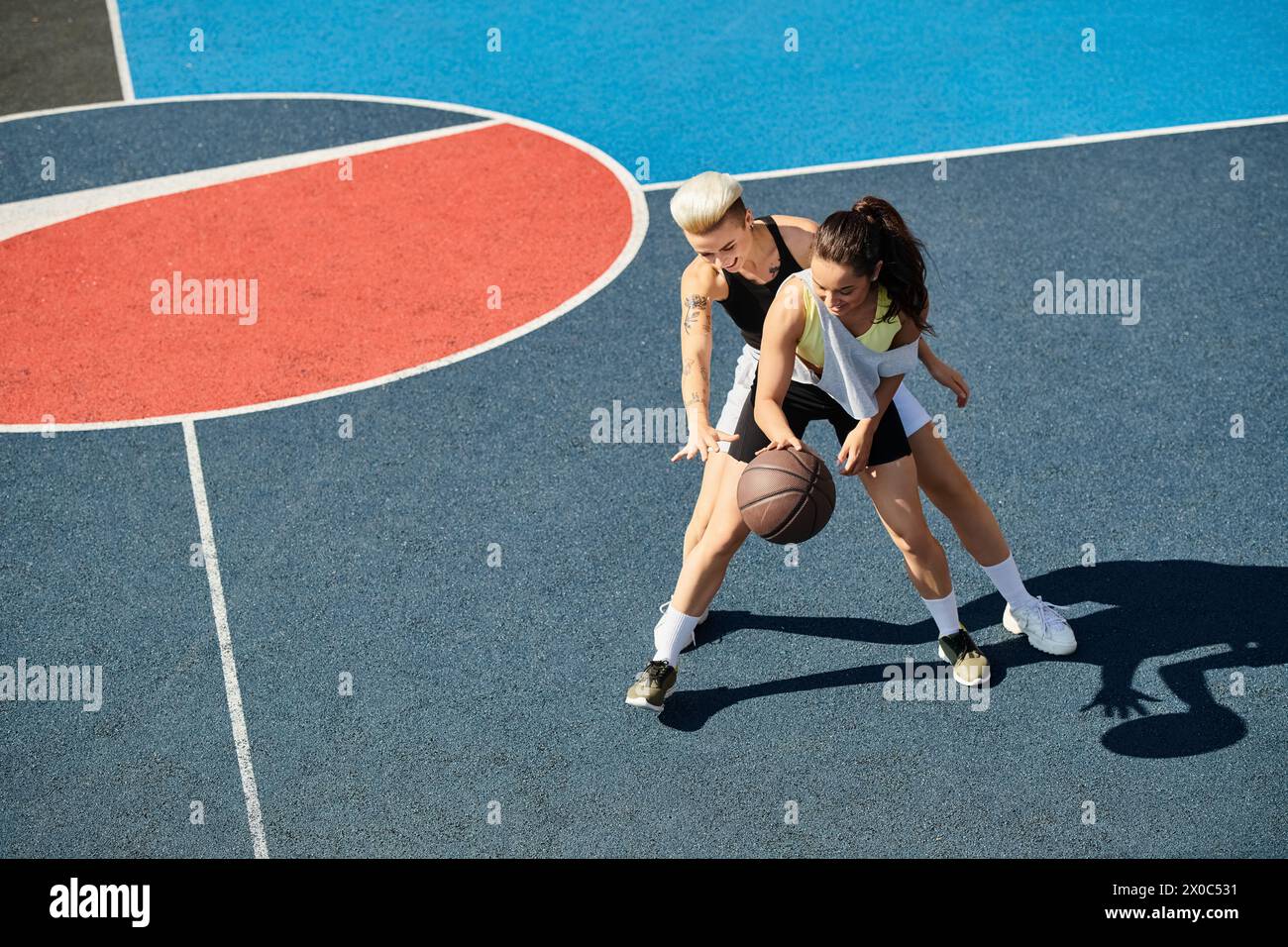 Due donne atletiche sono in piedi su un campo da basket, celebrando la loro amicizia e amore per il gioco in una giornata estiva di sole. Foto Stock