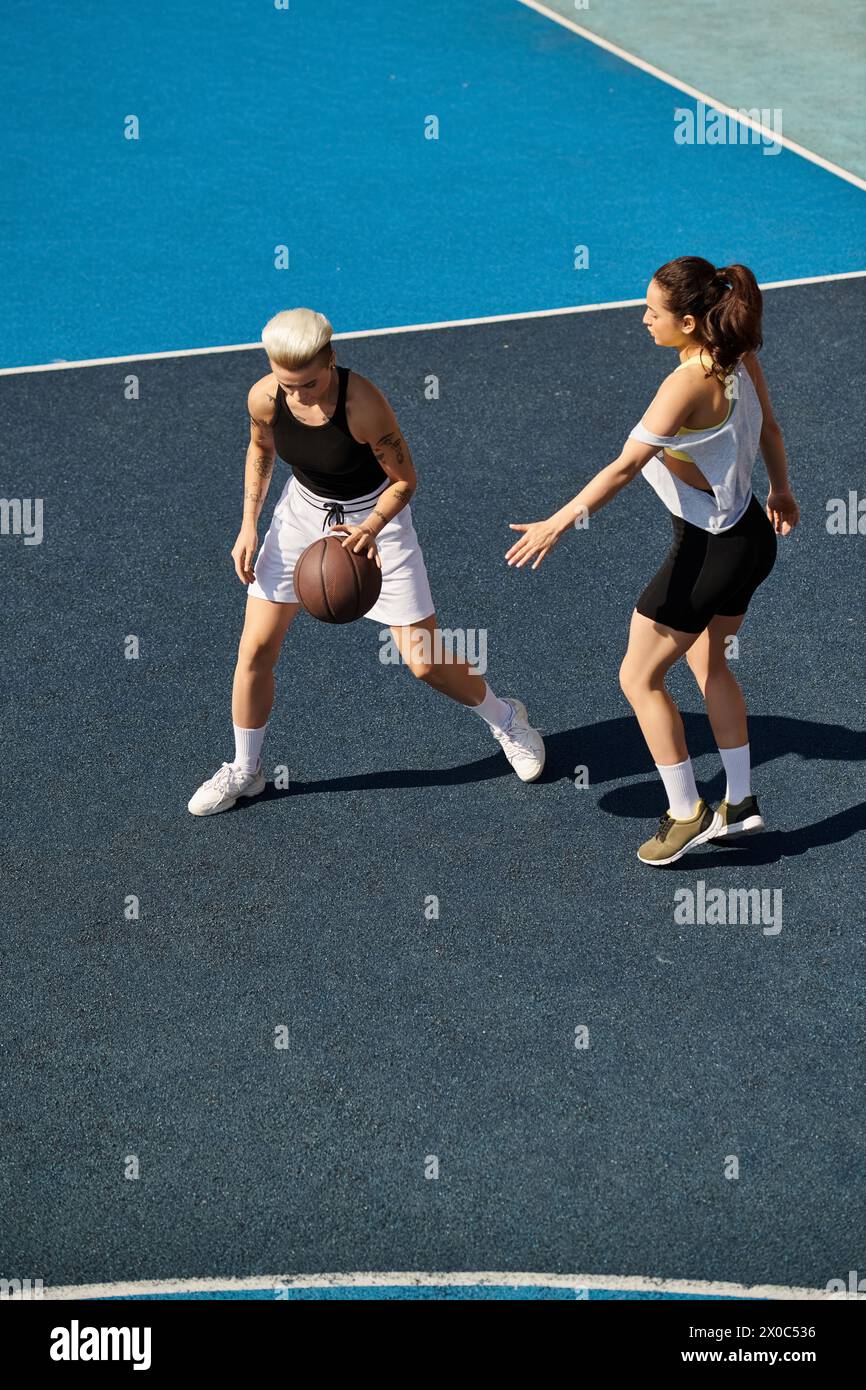Giovani donne atletiche che giocano a basket all'aperto in una giornata di sole, mostrando le loro abilità e il loro lavoro di squadra. Foto Stock