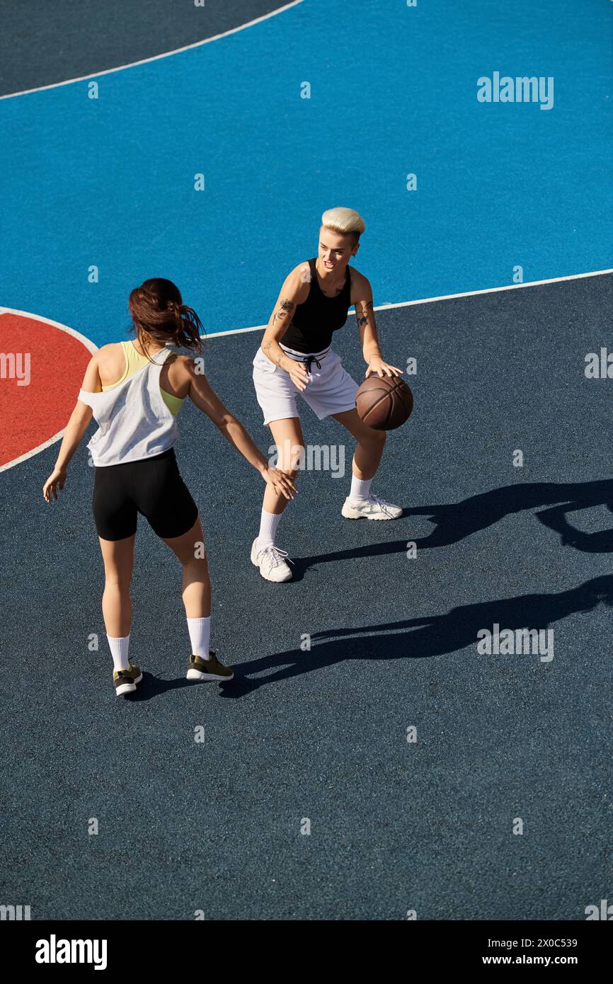 Due giovani donne si trovano in cima a un campo da basket, incarnando forza e lavoro di squadra sotto il sole estivo. Foto Stock