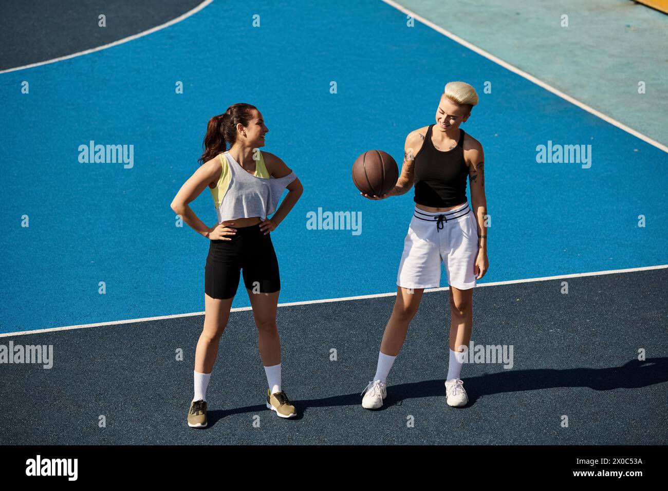 Due giovani donne atletiche, amiche, si alzano in piedi in sicurezza su un campo da basket, godendosi una giornata estiva. Foto Stock