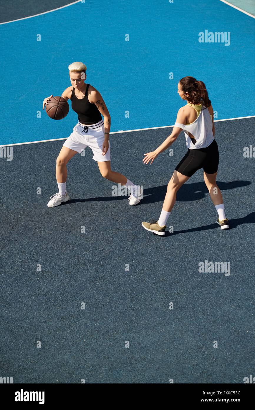 Due giovani donne, atletiche e competitive, giocano a basket su un campo all'aperto in una giornata estiva. Foto Stock