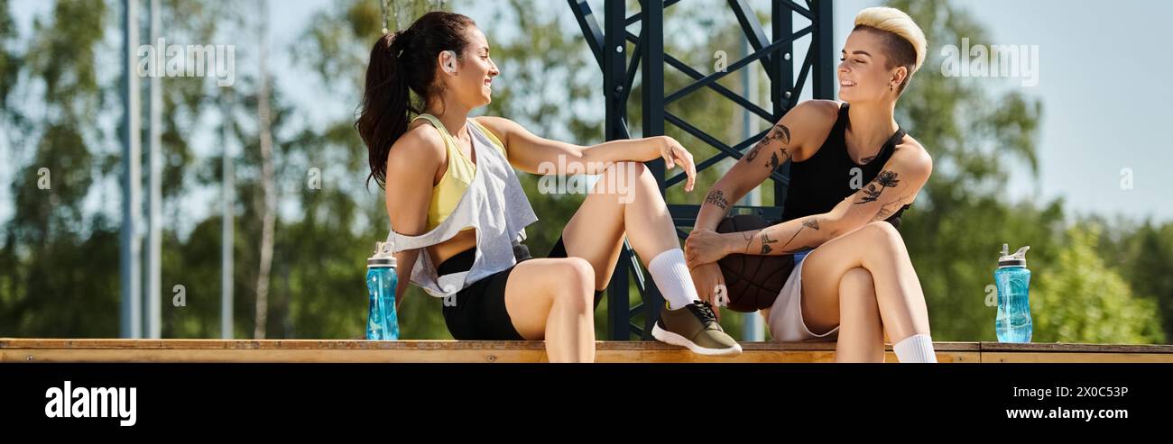 Due giovani donne, amiche, condividono un momento di cameratismo mentre sono sedute l'una accanto all'altra su un campo da basket all'aperto. Foto Stock