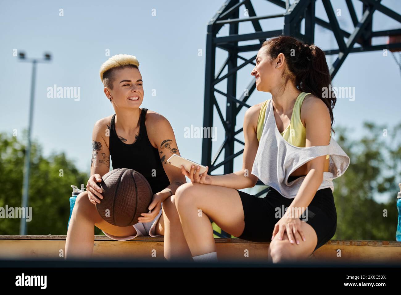 Due giovani donne, atletiche e ricche di vigore, trascorrono una giornata di sole all'aperto mentre si siedono a terra con una pallacanestro. Foto Stock