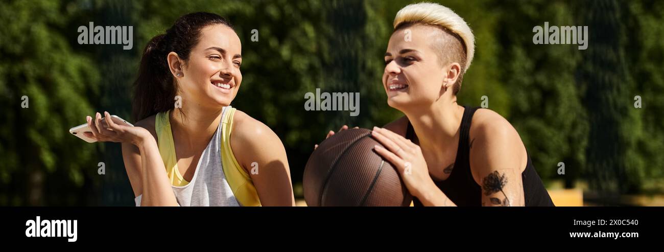 Due giovani donne, amiche e atleti, si alzano all'aperto per tenere una pallacanestro, mostrando il loro amore per lo sport. Foto Stock