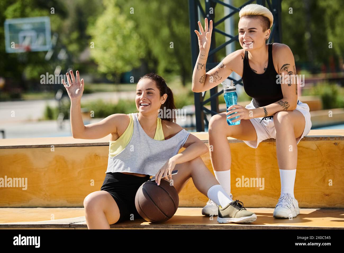 Un momento di serenità all'aperto, mentre due giovani donne siedono a terra, condividendo un pallacanestro in un'esibizione di cameratismo atletico. Foto Stock