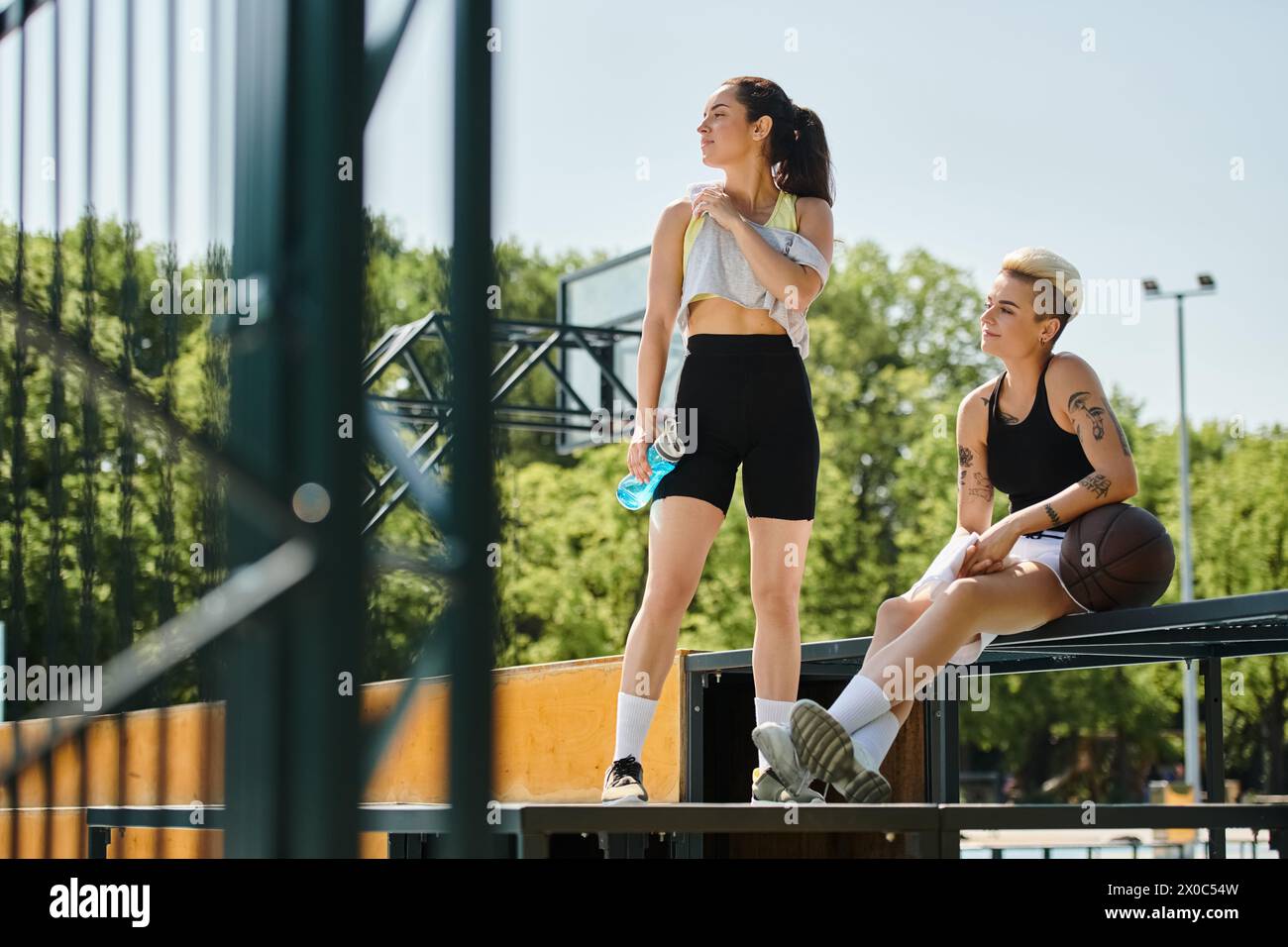 Giovani donne atletiche che si prendono una pausa dal basket, sedute in cima a una panchina sotto il sole estivo. Foto Stock
