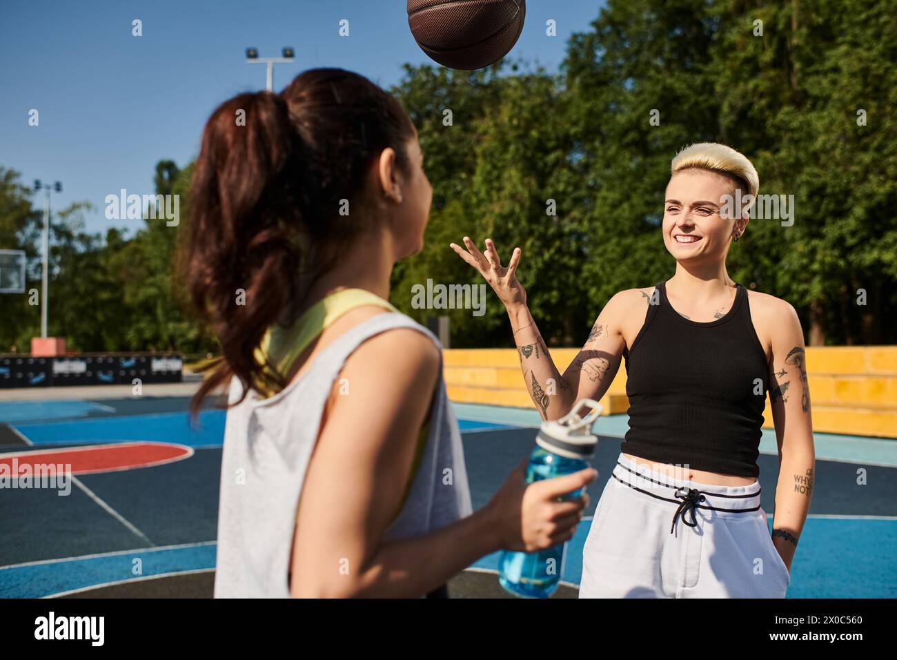 Una giovane donna si trova di fronte a una pallacanestro su un campo all'aperto soleggiato. Foto Stock