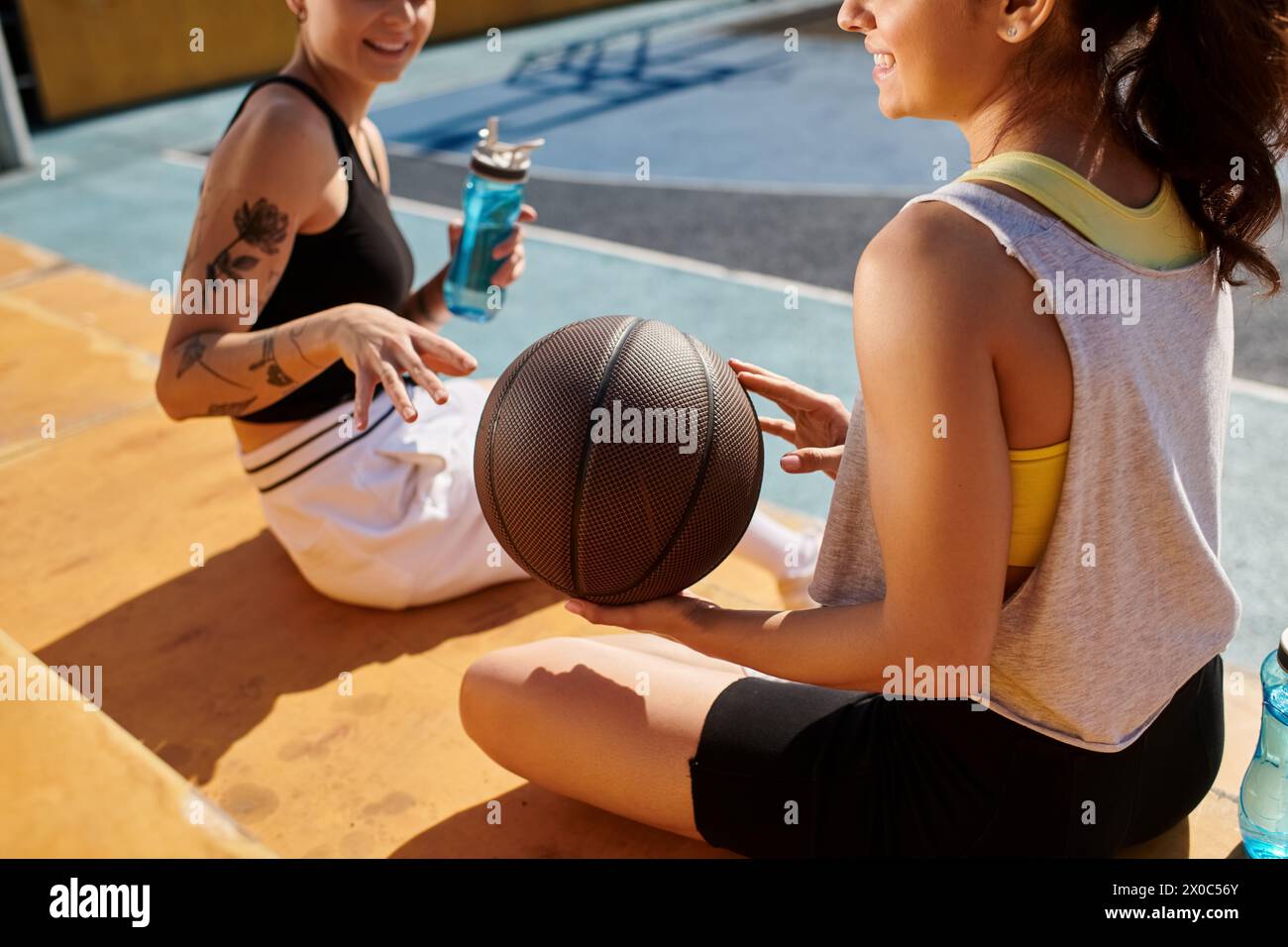 Due giovani donne, amiche atletiche, sedute fianco a fianco e con una pallacanestro all'aperto in una giornata di sole. Foto Stock