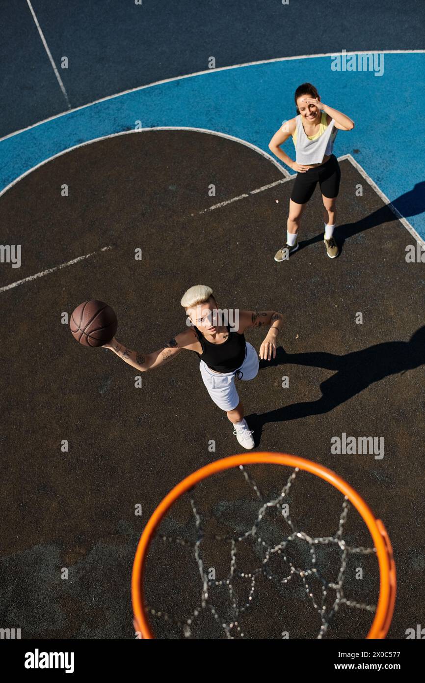 Due donne atletiche in azione su un campo da basket, dribbling, tiro e gareggiare in un gioco emozionante sotto il sole splendente. Foto Stock