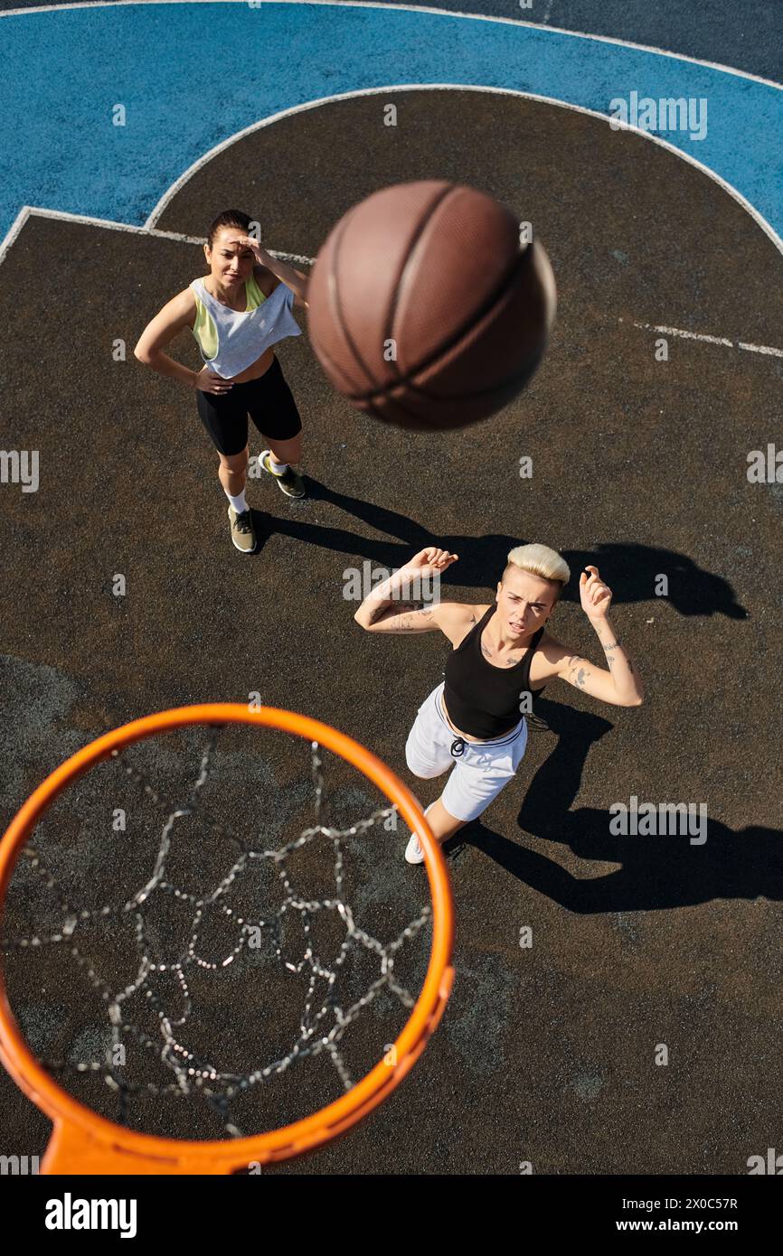 Due giovani donne, amiche, giocano a basket su un campo, mostrando le loro abilità atletiche in una partita estiva a canestro. Foto Stock