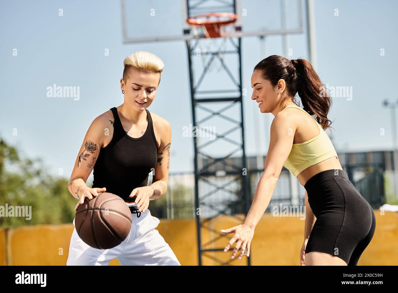 Due giovani donne stanno fianco a fianco all'aperto e tengono una partita di basket mentre giocano a canestro sotto il sole estivo. Foto Stock