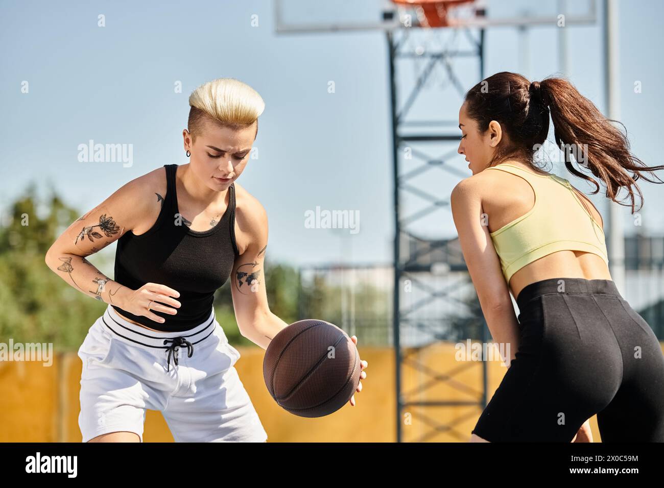 Una giovane donna che gioca energicamente a basket su un campo soleggiato all'aperto, mostrando il proprio atletismo e il proprio lavoro di squadra. Foto Stock