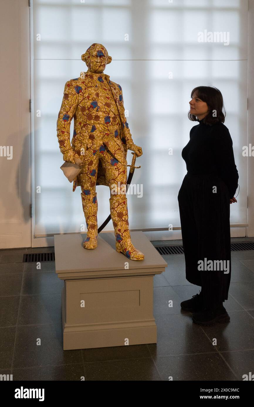 LONDRA, REGNO UNITO - 11 APRILE 2024: Un membro dello staff guarda "Clive", "Decolonized Structures" (2022-23), composto da sette sculture in vetroresina di figure coloniali, dipinte a mano con motivo a cera olandese durante un photocall per la mostra "Suspended States" di Yinka Shonibare a Serpentine South a Londra, Regno Unito, l'11 aprile 2024. La prima mostra personale del lavoro di Shonibare in un'istituzione pubblica di Londra da oltre 20 anni esplora i temi centrali delle eredità del potere coloniale, dei siti di rifugio e rifugio, nonché l'impatto ecologico della colonizzazione, l'eredità europea dell'imper Foto Stock