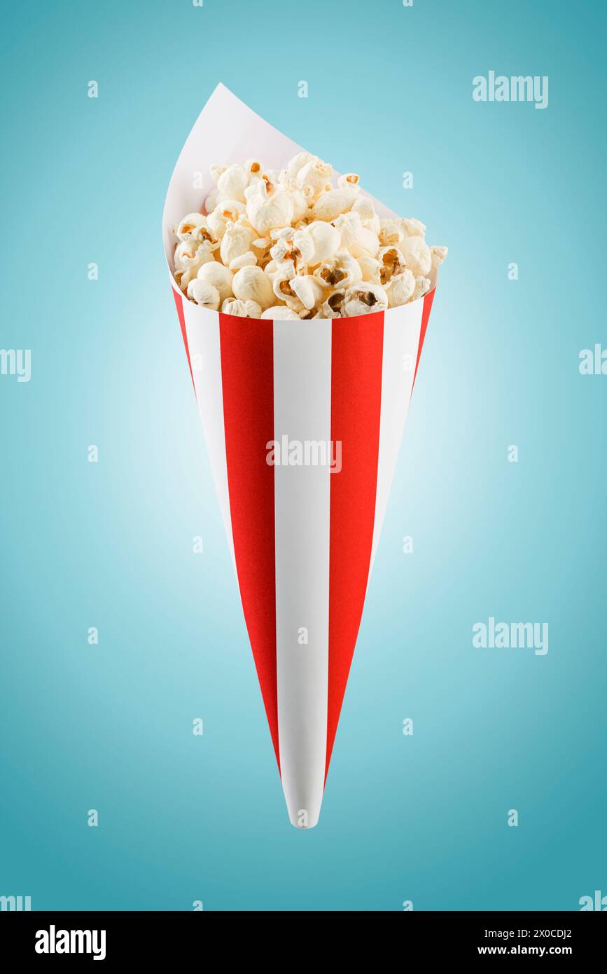 Popcorn con cono di carta a strisce rosse e bianche su sfondo blu. Foto Stock
